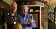 Former Olympic champions Bill Lienhard, left, and Charlie Hoag, show their gold medals in front of the KU Olympian display at the Booth Family Hall of Athletics on Monday at Allen Fieldhouse.