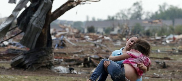 A woman carries a child through a field near the collapsed Plaza Towers Elementary School in Moore, Okla., Monday, May 20, 2013. The relationship between the woman and the child was not immediately known. A tornado as much as half a mile (.8 kilometers) wide with winds up to 200 mph (320 kph) roared through the Oklahoma City suburbs Monday, flattening entire neighborhoods, setting buildings on fire and landing a direct blow on an elementary school. (AP Photo Sue Ogrocki)