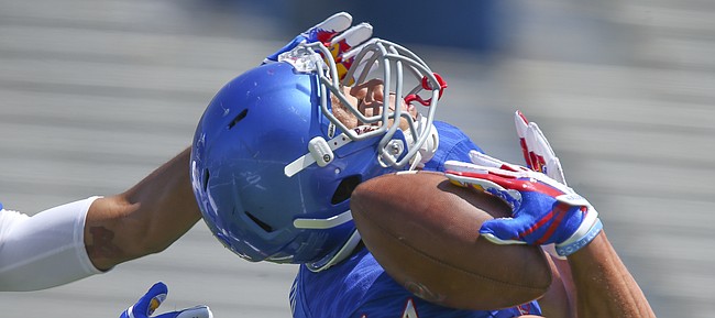 Kansas wide receiver Kerr Johnson Jr. (14) hangs on to a deep catch on his shoulder pad as cornerback Corione Harris reaches for him during an open practice on Saturday, April 28, 2018 at Memorial Stadium.