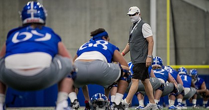 Kansas football head coach Les Miles wears a mask while walking around during an early August practice in the team's indoor facility.