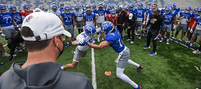 Members of the Kansas football team circle up to watch teammates battle through a drill during a spring practice at David Booth Kansas Memorial Stadium, in April of 2021.