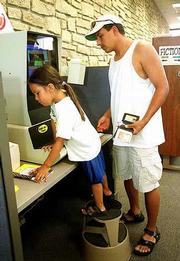 Mia Monteau, 4, uses a self-checkout machine with her father
Maurice, Lawrence, Friday in the childrens area of the Lawrence
library. A new automatic reader for the adult section of the
library should arrive in September soon after a renovation to
replace the laminate counters now in the circulation department.