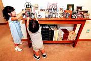 Tia, 3, and Rider, 2, inspect a table of framed pictures that
displays family photographs and the original snapshots the Comptons
received on each of their six adopted children.