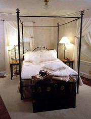 This bedroom features a white-on-white decorating theme with soft
sheer fabric at the windows and layers of creamy bed coverings and
pillows on the bed. Wrought-iron accents add contrast.
