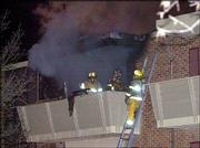 Firefighters tackle the third-floor fire from a balcony. Shortly
after firefighters arrived, an explosion tore much of the brick and
front of the burning apartment away. The explosion was caused by an
oxygen canister.
