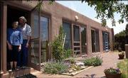 Barbara and Fred Raznick stand in a back door of their passive
solar home in Eldorado, N.M. Floor-to-ceiling windows along the
south side of the home allow sunlight inside the 22-foot-wide home
in the winter, while keeping it out in the summer.