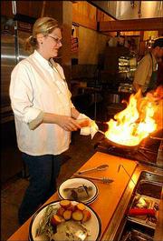 Janna Traver, a Kansas University graduate and Lawrence resident,
fires up a brandied demi-glaze to finish off a peppered elk chop at
Cabela's.