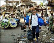 Unidentified foreign tourists carry their luggage past the site of
a bomb blast at Kuta Beach on the Indonesian island of Bali. More
than 180 people, most of them foreign tourists, were killed and
hundreds were injured when a pair of bombs exploded Saturday night
in the nightclub district.