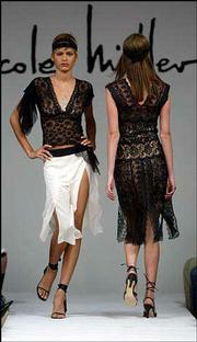 A black V-neck lace top with asymmetric mesh handkerchief pieces is
modeled over a white georgette panel skirt with black yoke during
the showing of the Nicole Miller Spring 2003 collection in New
York. At right is a black lace strip dress with nude slip. The
slinkier look of the bedroom is increasingly becoming part of
everyday street fashion.