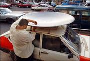 An Iraqi man ties a newly purchased satellite dish to his car in
downtown Baghdad. Satellite television, which was banned during
Saddam Hussein's regime, is now in big demand in Iraq.