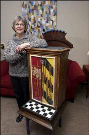 Joelle Ford creates whimsical furniture and assemblages out of
mostly wooden odds and ends she scavenges at antique malls, flea
markets and garage sales. She's pictured with a music cabinet
constructed of parts from at least four different pieces of
furniture, tiles, paint, fabric and wallpaper border. It and the
painting behind her will be part of a show opening Wednesday at the
Lawrence Arts Center.