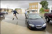 Something new in normally dry Johnson City: rain. Congressman Jerry
Moran jumped the six-foot-stream of water running down the city's
main street to get to his car. Garden City Telegram reporter Scott
Aldis-Wilson watches the congressman in action.