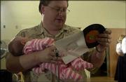 Kevin Oneslager, of Lawrence, the caller for the Tons of Fun square
dancing club, holds his 1-month-old daughter, Kimberly, while
getting a record ready for the next dance.