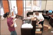 While Edwards Campus staff Reena Thomas, lab assistant, foreground
left, and Maureen Raymond, adminstration, right, organize the front
reception desk at the new Regnier Hall, Rick Hunter, Lawrence, an
employee with Kennedy Glass, Lawrence, background left, finishes
some work on a door. The new hall opens Monday.