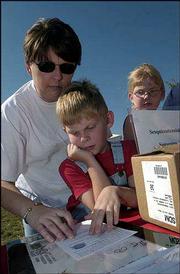 From left, Michele Schneck, Lawrence, and her son Eli, 7, and
daughter Karey, 8, fill out postcards to include in the
Sesquicentennial Time Capsule. The capsule was buried Sept. 19 at
Sesquicentennial Point near Clinton Lake Dam during the closing
ceremony of Lawrence's birthday celebration.