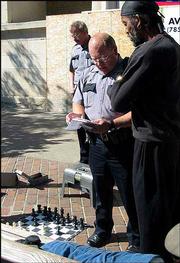 Lawrence Police officers give Sherman "Sly" Talbert a warning about
blocking the sidewalk with chess boards. Players now must confine
their games to a bench at the corner of 10th and Massachusetts
streets.