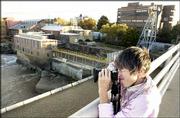 Photographer Carolyn Young, Lawrence, composes a photo on the
Massachusetts Street Bridge. The Bowersock Mills and Power Co.,
pictured at center, received an accreditation that will allow the
company to start charging a premium for its renewable energy.