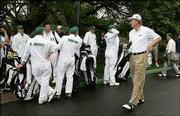 Golfer Ernie Els walks past caddies gathered in front of the
clubhouse after rain suspended play Friday at Augusta National in
Augusta, Ga. The golfers will attempt to play the second and third
rounds today, weather permitting.
