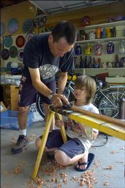Bob Gent and his son, Ian, 10, work on a wooden sword Thursday in their workshop. Gent, a local glass artist, raises two kids, Ian and Helen, 13.