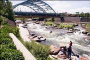People watch from the banks of the South Platte River as a couple of kayakers make their way through the white water. The river is a short distance from the western end of 16th Street, across the Millennium Bridge.