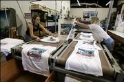 Rian Busse, left, and Brenda Mulberry take Discovery launch T-shirts off the conveyor dryer Thursday at Space Shirts in Merritt Island, Fla. The area's 9,000 hotel rooms are all booked and T-shirts have been delivered to local shops.