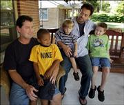 Bill Dunn, left, holds Haden, 5, while Shaun Morse holds Henry, 2 , and Nathan, 6, on the front porch of their home in Wichita. Both Dunn and Morse are listed as parents of the California adopted boys. Kansas state law is silent on whether gays or lesbians can adopt foster children.