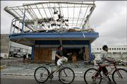 Bicyclists pass a store Sunday destroyed by Hurricane Wilma in Cancun, Mexico. Police in Cancun tried to protect both stores and foreign tourists from the looters, and the military set up checkpoints to seize stolen goods.