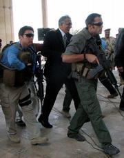 U.S. Ambassador to Iraq Zalmay Khalilzad, center, is escorted by armed guards Tuesday soon after insurgents fired a mortar at a U.S. ceremony, sending the U.S. ambassador scrambling for cover but causing no injuries in Tikrit, Iraq.