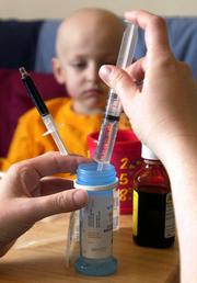 Christian Faulkner watches in the background as his mother, Amanda, prepares syringes used to flush the lines of his feeding tube. Medical treatments to cure cancer have reduced Christian's weight to about 38 pounds, and his parents are hoping that he can quickly gain back his weight so his feeding tubes can be removed.