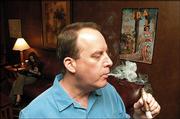 Rich Spangler, co-owner of Centro Cigars, 1520 Wakarusa Drive, lights up one of his favorites in the shop's lounge, Club Centro. The business, which includes a walk-in humidor, top right, with more than 2,000 cigars, is exempted from the city's smoking ban.