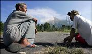 Villagers chat as they watch Mount Merapi, background, releasing volcanic gas in Deles, Central Java, Indonesia. Scientists warned that the erupting volcano still posed a deadly threat to villagers living on its lava-scarred slopes, as a bout of intensified activity was recorded on Wednesday.
