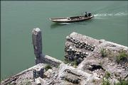 A Chinese man powers his boat past the remains of an old town partially covered by the rising water of the Yangtze River just upriver of the Three Gorges Dam. Authorities are expected to announce the completion of the main wall of the dam Saturday, months ahead of schedule.