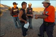 Carlos Estrada, a police agent working with the Mexican government's migrant assistance unit, Grupo Beta, distributes packets of rehydration powder to a group of migrants last week in the desert near San Luis Rio Colorado, Mexico. Left to right are Porfiro Vera Jimenez, 19, Cesar Garcia Vazquez, 23, and Hugo Sanchez Martinez, 19.