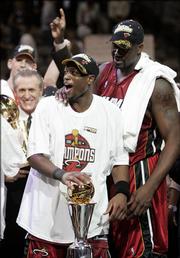 As center Shaquille O'Neal, right, and head coach Pat Riley, background, look on, Miami guard Dwayne Wade holds his MVP trophy after the Heat clinched their first NBA title. Miami secured the championship with a 95-92 victory over Dallas in Game 6 of the NBA Finals on Tuesday night.