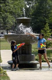 Joseph Cliff, 9, and his sister, Iris Cliff, 14, both of Lawrence, play around the fountain Thursday in South Park. The city shut down the fountain during Wednesday evening's city band concert because it's a magnet for children, who might get hurt climbing in and around it.