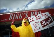 Warren Elliott, A Kansas University junior from Salina, displays a marketing costume and sign that soon will be retired from Bigg's Bar & Grill, 2429 Iowa. The days are numbered for the promotion, which the bar's owner had used for the past year, playing off a Chick-fil-A ad.