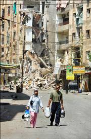 A couple carrying some of their salvaged belongings walk through a destroyed street Saturday in the southern suburbs of Beirut, Lebanon. After more than a week of sustained Israeli airstrikes on the previously densely populated, Hezbollah-controlled area of the capital, few civilians remain, though some ventured back Saturday to salvage belongings.