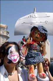 A demonstrator wearing a mask meant to represent U.S. Secretary of State Condoleezza Rice and holding a doll smeared in fake blood joins more than 2,000 Syrian women in a protest in Damascus. The protesters, most of them dressed in black, carried coffins wrapped in black proclaiming the death of peace and the birth of a new Middle East. Placard reads: New Middle East.