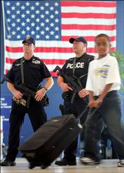 A traveler passes in front of police officers with automatic weapons at JFK International Airport in New York. U.S. passengers are facing heightened security at airports after authorities in London uncovered a terror plot aimed at airlines traveling from Britain to the U.S. Security screening lines grew long and slow-moving as passengers got special inspections, and drinks and most other liquids and gels were banned as carry-on items.