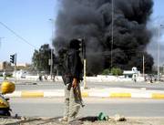 A masked gunman stands on a street corner as a building burns nearby Friday in the southern Iraqi town of Amarah, Iraq. Mahdi Army, the Shiite militia run by anti-American cleric Muqtada al-Sadr seized control of the southern Iraqi city of Amarah on Friday after their fighters stormed three main police stations, planting explosives that flattened the buildings.