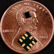 The mechanical part of a motion-sensing chip used in the controller for Nintendo Co.'s Wii game console is near the top of a penny to illustrate its size. The chip, made of silicon using the same techniques that produce electronic chips, contains two spring-loaded weights and is packaged with an electronic component into the larger assembly seen on the lower part of the coin. The chip is supplied by STMicroelectronics NV.
