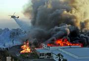 The former Egg City facility and an adjacent warehouse are engulfed in flames as a helicopter dumps water on the fire in Moorpark, Calif., on Sunday. A fire driven by strong winds Sunday destroyed five homes and a storage building and endangered hundreds of others in canyons and hillsides, authorities said.