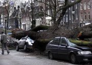 A man passes by two cars crushed by an uprooted tree during storms Thursday in Amsterdam, Netherlands. Northern Europe began cleaning up Friday after Thursday's deadly storm.