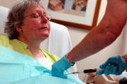 With her eyes closed in a "here we go again" expression, Kathy's port, implanted in her chest, is flushed before her chemotherapy cisplatin is administered.