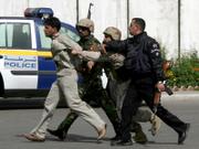 Iraqi policemen lead a man away from a building in Baghdad, Iraq, where an explosion took place. Iraqi Vice President Adel Abdul-Mahdi escaped an apparent assassination attempt Monday after a bomb exploded in municipal offices where he was making speech, knocking him down with the force of the blast that killed at least 10 people.