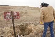 A bullet-ridden sign warns passersby, including Randy Johnson, of an open mine shaft leading to hundreds of feet into the ground near Galena, Kan. The old mining areas in southeast Kansas are covered with these holes.