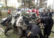 Police look for evidence in a car that exploded next to a police station, seen in background in Algiers, Algeria. Bombs ripped through the Algerian prime minister's office and a police station, coordinated terror attacks that authorities said killed at least 24 people and wounded more than 200 others.