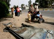 An Iraqi family walks past a car part after a car bomb exploded near Baghdad University. A troop surge intended to quell violence in the Iraqi capital has stretched the U.S. Army thin, and on Wednesday it was announced that troops would have to spend an additional three monts in Iraq.