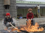 Sisters Celie Davison, 10, left, and Bess, 6, burn wood as their father, Doug Davison, repairs a roof at his Vinland Valley Nursery. The two girls and their older sister, Emma, 11, are home schooled by their parents and between studies the girls help out around the nursery.