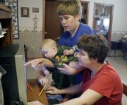Donna Thomasson enters a grade into the Lawrence Virtual School computer system as her son Luke looks on and holds his brother, 5-month-old Chip. The school day usually lasts from 8:30 a.m. to around noon for the Thomassons.